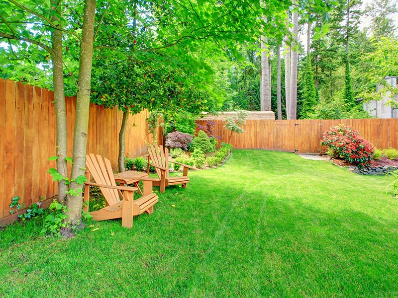 This is an image of a green lawn with wooden chairs. LandTech Landscaping specializes in landscaping maintenance and lawn care similarly to how it's shown here.